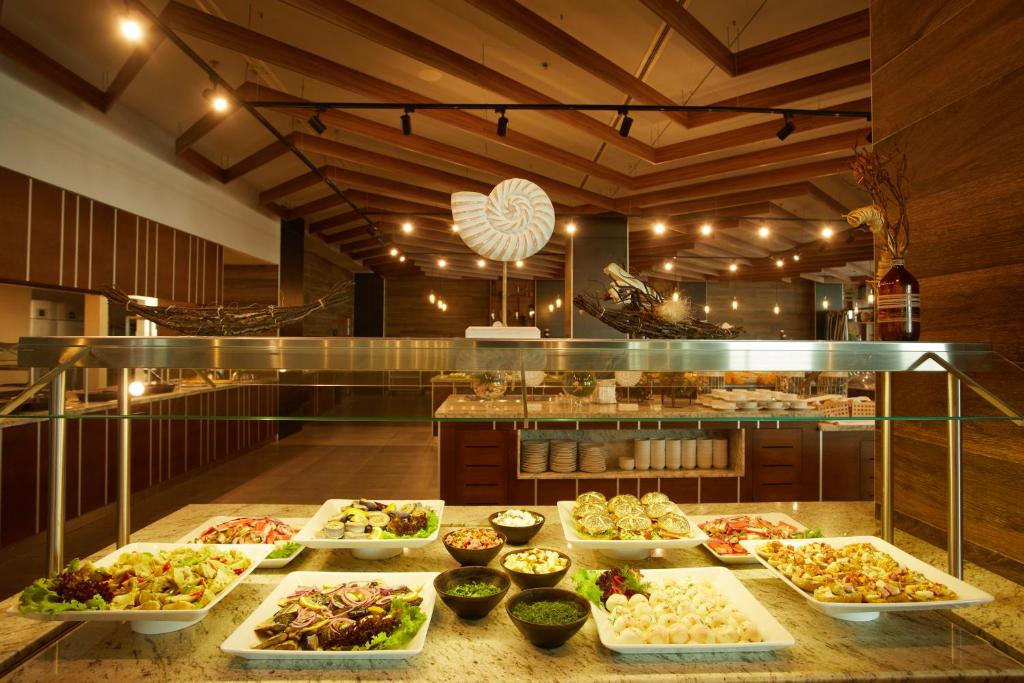 Gardi salāti un dažādi ēdieni izkārtoti bufetē modernā restorānā ar koka griestiem un siltu apgaismojumu.