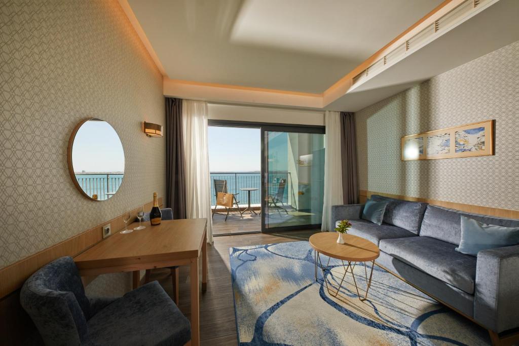 Mūsdienīga viesnīcas numura interjers ar jūras skatu, ērtiem mēbeļu risinājumiem un apgaismojumu. Numurā ir balkons un viesu sēdvietas.