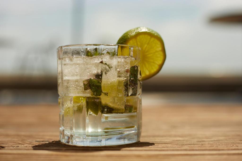 Atspirdzinošs kokteilis ar laima un piparmētru, pasniegts stikla glāzē uz koka virsmas.