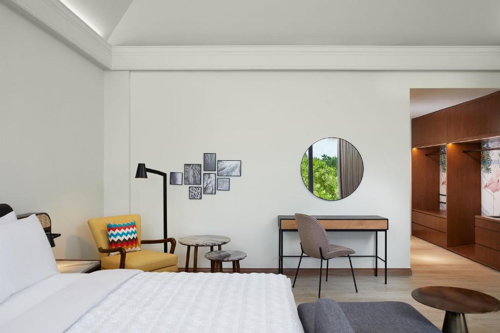 Mūsdienīgs guļamistabas interjers ar ērtu gultu, krāsainu krēslu un galdu, kā arī dekoratīvām gleznām uz sienas un lielu spoguli. Telpa ir gaiša un plaša, radot patīkamu atmosfēru.