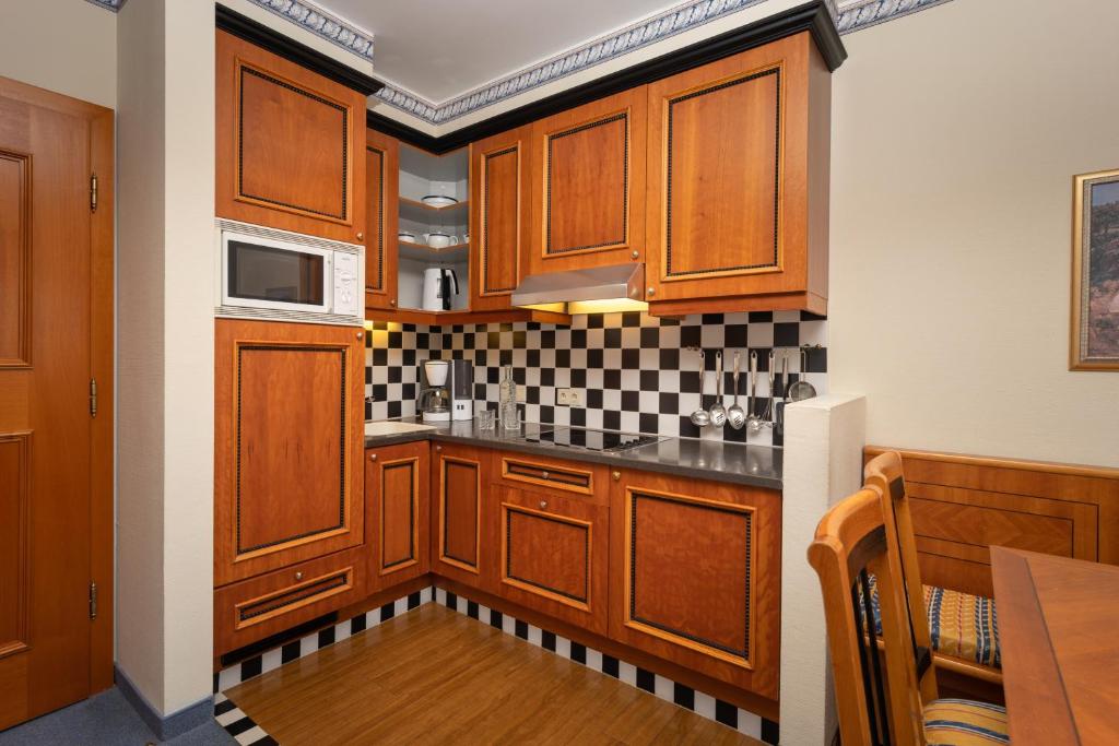 Kompaktā virtuve ar koka skapjiem un melnbaltu flīžu apdari, aprīkota ar mikroviļņu krāsni, kafijas automātu un galdu.