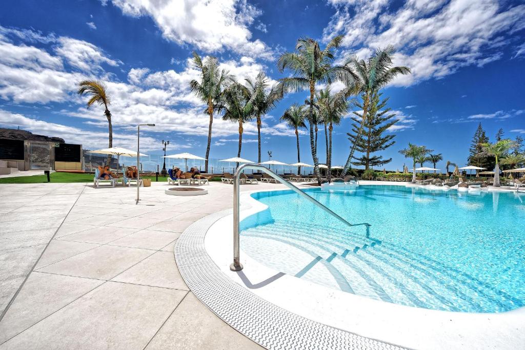Peldbaseins ar palmām un skaidru zilu debesi, kas rada relaksējošu tropisko atmosfēru. Ideāla vieta atpūtai un brīvā laika pavadīšanai.