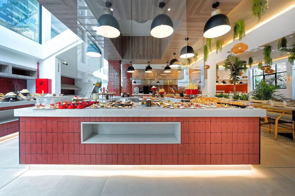 Moderns bufetes stils restorāns ar plašu ēdienu izvēli, iekārtots ar stilīgām lampām un augiem, radot patīkamu atmosfēru.
