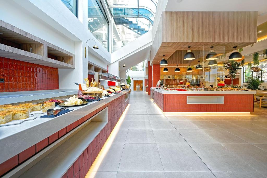 Grezns bārs ar plašu ēdienu izvēli, kas iekārtots modernā stilā ar sarkaniem un pelēkiem toņiem. Gaismas un stikla elementi rada patīkamu atmosfēru.