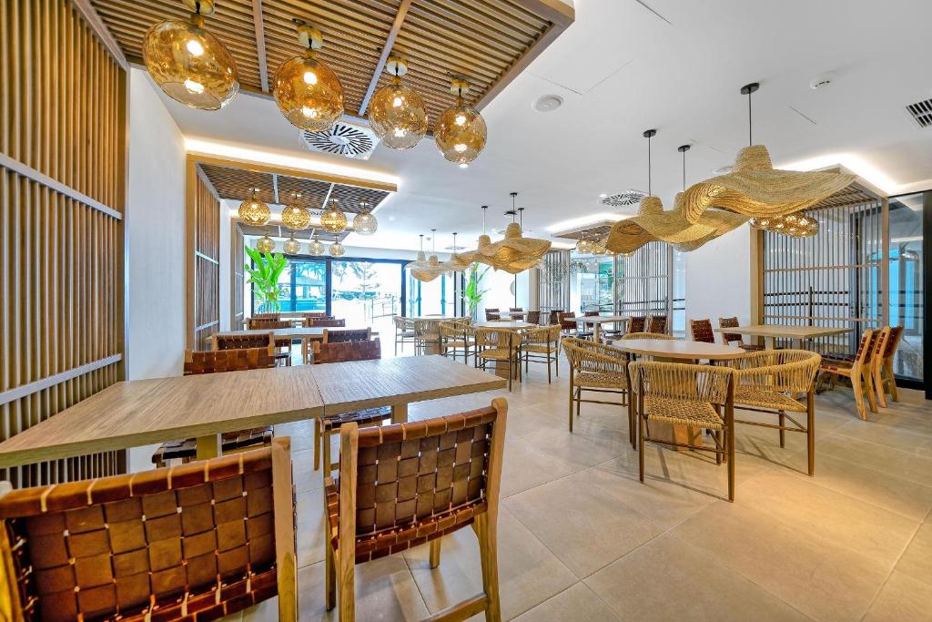 Modernā restorāna interjers ar koka mēbelēm, stilīgām gaismām un augu akcentiem. Plašs, gaišs un elegants telpas dizains, kas rada patīkamu atmosfēru.