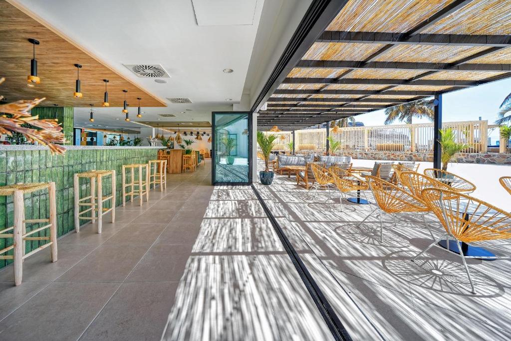 Mūsdienīgs bārs ar zaļām flīzēm un rattan krēsliem, kas piedāvā ērtu atpūtu zem jumta. Gaismas un ēnas spēle rada patīkamu atmosfēru.