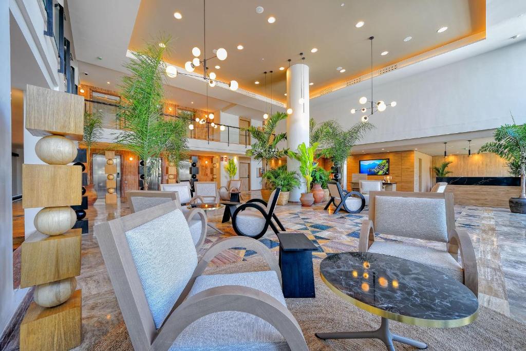 Mūsdienīgs viesnīcas vestibils ar augstiem griestiem, dabīgām augu dekorācijām un modernu mēbelēm, izveidojot elegantu un relaksējošu atmosfēru.