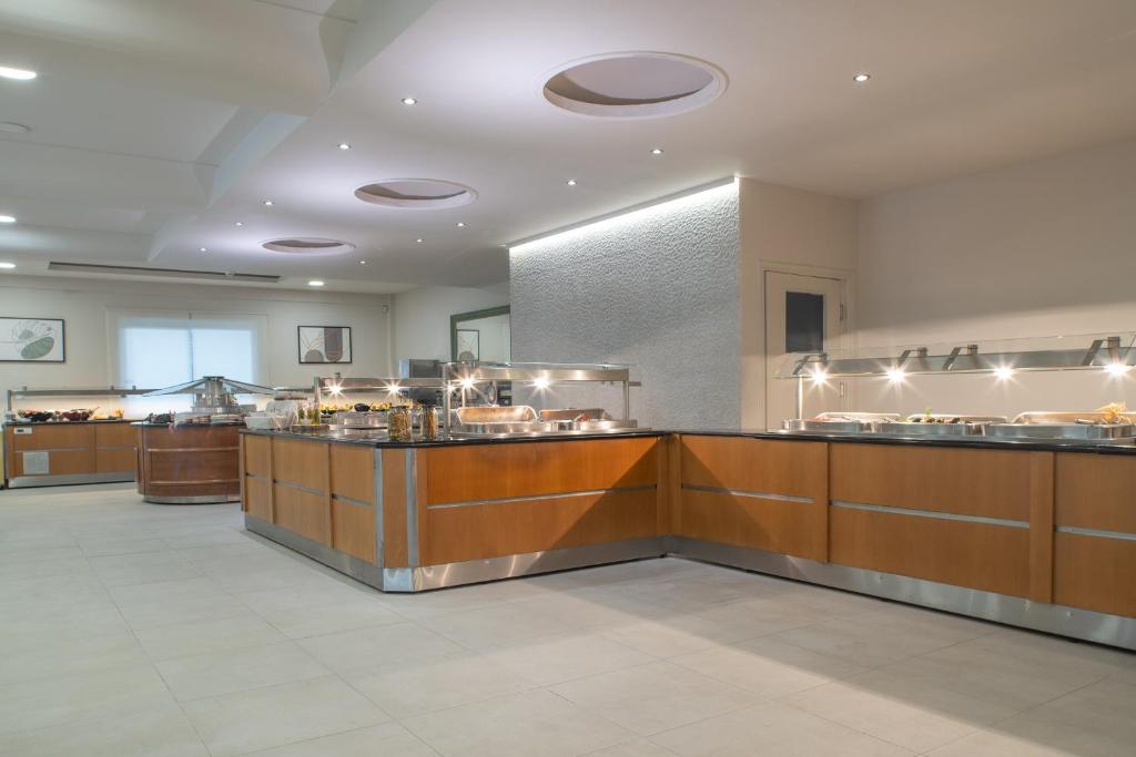 Mūsdienīgs bufetes stils ar koka un metāla elementiem, kas ietver dažādu ēdienu izvēli. Apgaismojums un plašs interjers rada viesmīlīgu atmosfēru.