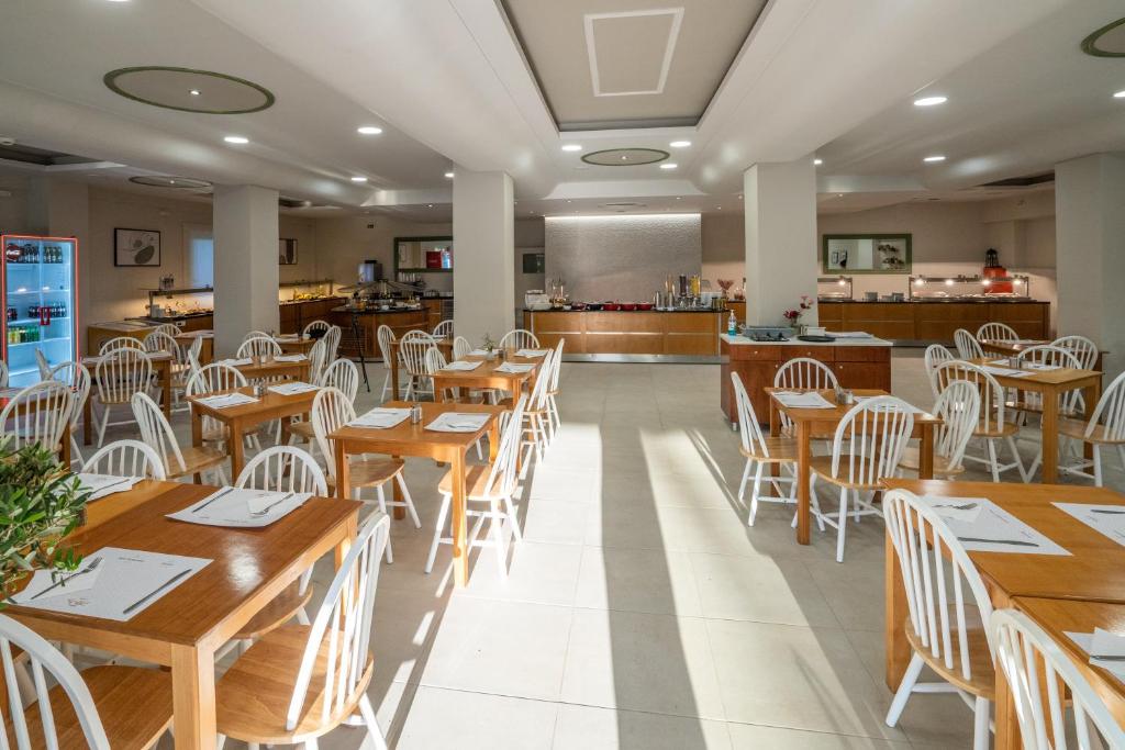 Gaiša un moderni iekārtota restorāna iekšiene ar koka galdiem un baltiem krēsliem, kurā redzami galdi ar ēdienu izvēlni. Restorānā ir arī bufete un dzērienu ledusskapis.
