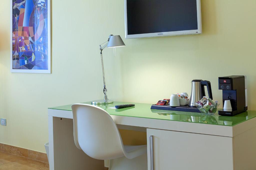 Moderna darba vieta ar zaļo galdu, lampu un kafijas automātu, papildināta ar krēslu un televizoru uz sienas.