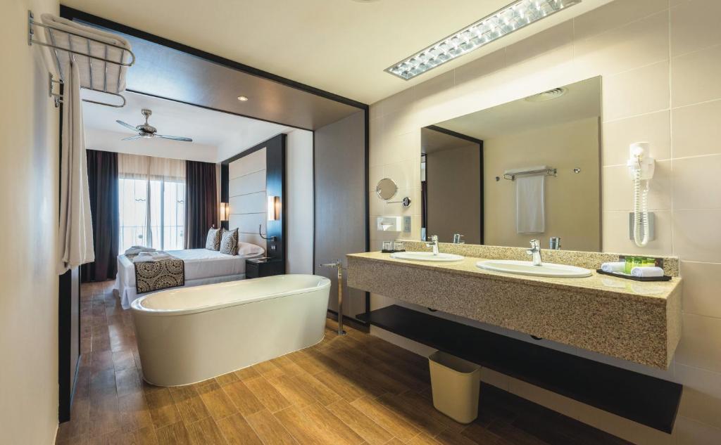 Mūsdienīga viesnīcas numura un vannas istabas interjers ar elegantu vannu un divām izlietnēm, kas izceļas ar modernu dizainu un koka grīdu.