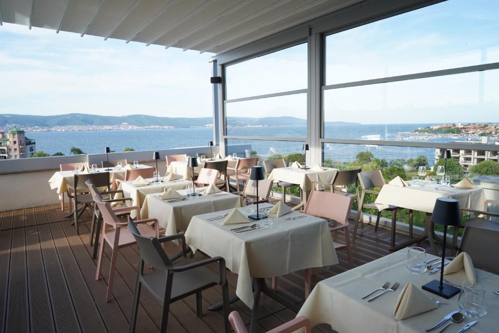 Moderns restorāns ar panorāmas skatu uz jūru, kur galdi ir klāti ar elegantiem galdautiem un galda piederumiem. Terase piedāvā patīkamu atmosfēru un dabas skaistumu.