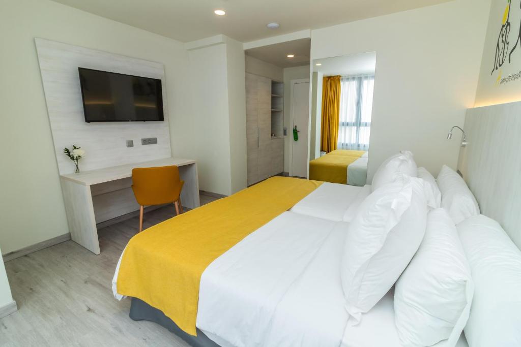 Mūsdienīga viesnīcas istaba ar dzeltenu gultas pārklāju, televizoru un rakstāmgaldu. Logi ar dzeltenām aizkariem piešķir telpai gaisīgu atmosfēru.