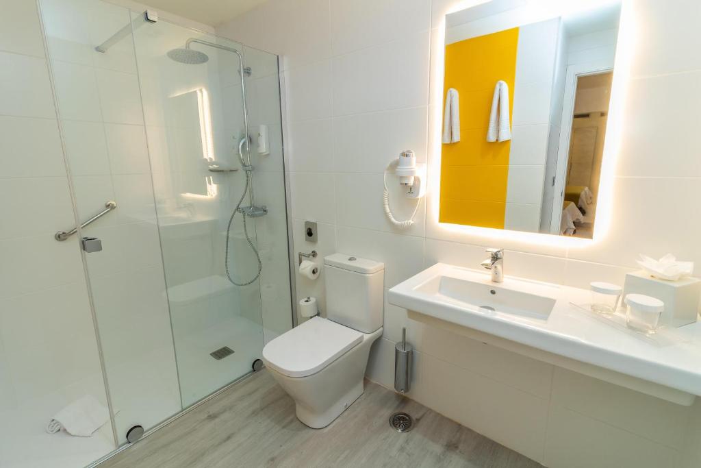 Mūsdienīgs vannas istabas interjers ar dušas kabīni, tualeti un izsmalcinātu izskatu. Gaismas spogulis un dzeltena akcenta siena piešķir telpai svaigumu.