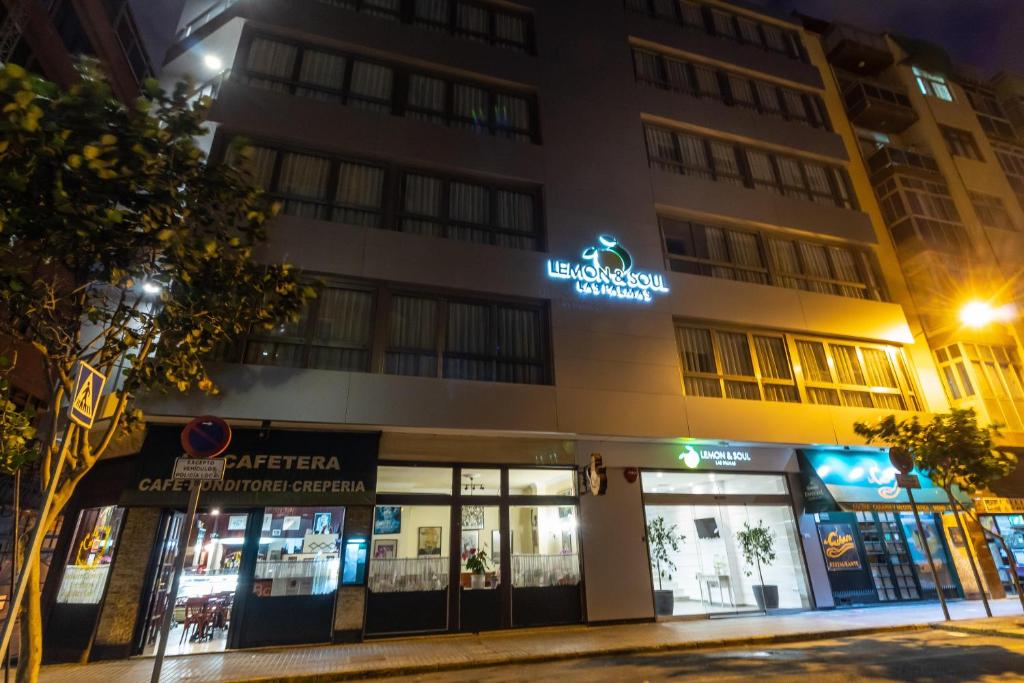 Moderns viesnīcas ēkas fasāde ar izgaismoto "Lemon & Soul" zīmi, kas atrodas naktī. Blakus ir kafejnīca un citi veikali.