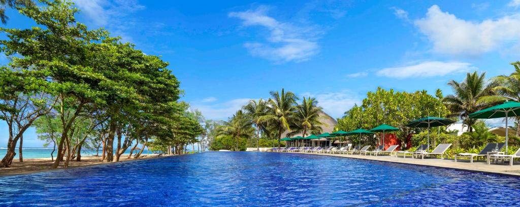 Lieliska ainava ar mirdzošu zilo baseinu, ko ieskauj zaļi koki un palmas, radot relaksējošu kūrorta atmosfēru. Ideāla vieta atpūtai pie ūdens.