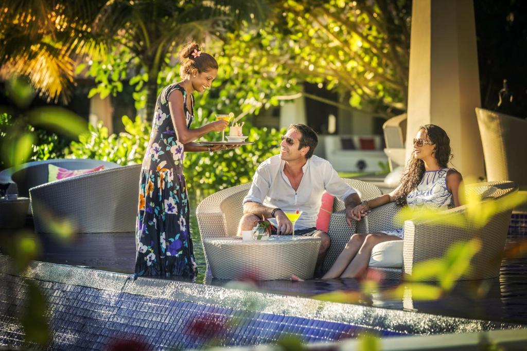 Pāris atpūšas pie baseina, baudot dzērienus, kamēr viesmīle pasniedz ēdienus. Apkārt ir zaļa daba un ekoloģiska atmosfēra.