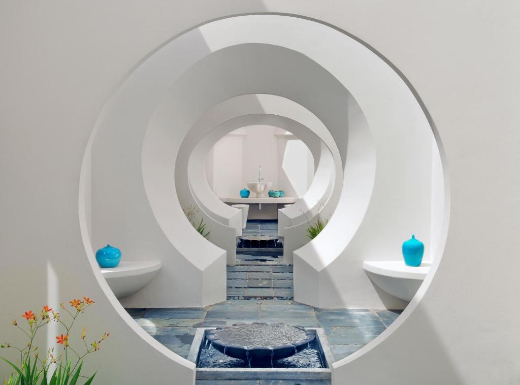 Mūsdienīga arhitektūra ar apaļām nišām un zilām dekoratīvām traukiem, kas veido mierīgu un estētisku vidi. Fons ar akmens grīdu un ziediem pievieno dabīgu šarmu.