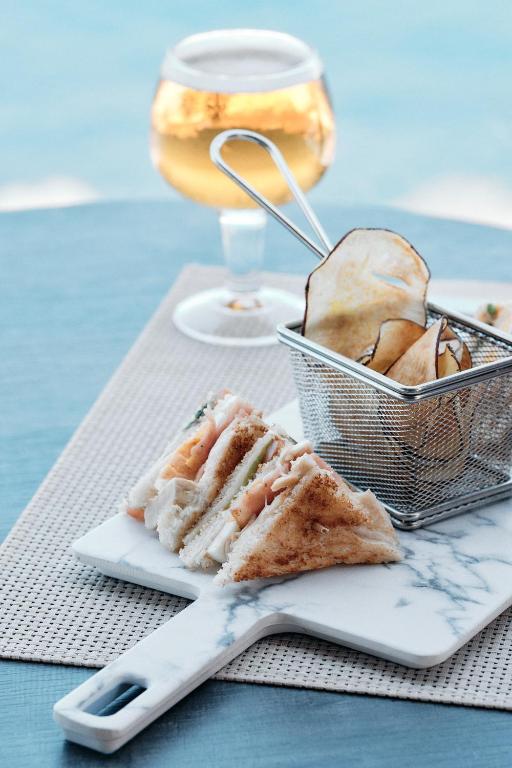 Svaigi pagatavota sviestmaize ar zivīm un dārzeņiem, pasniegta uz marmora šķīvja kopā ar kraukšķīgām kartupeļu čipsiem un dzērienu.