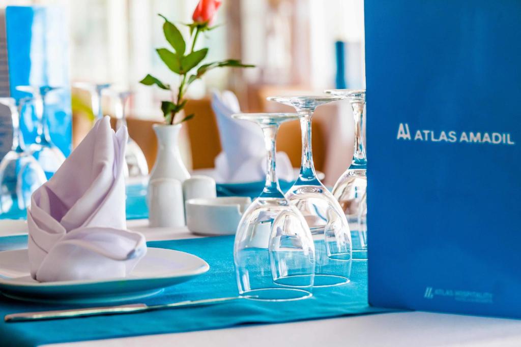 Elegants restorāna galdiņš ar zilu galdautu, baltām salvetēm un glāzēm, kā arī ziedu dekorācija. Redzams restorāna ēdienkarte 