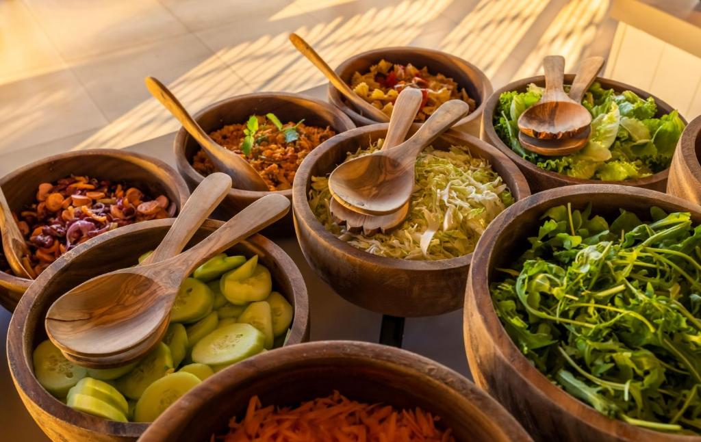 Koka bļodās ir dažādi dārzeņi un salāti, tostarp gurķi, kāposti un zaļumi, ar koka karotēm. Šī krāsainā un veselīgā sastāvdaļu izlase ir ideāla svaigu salātu pagatavošanai.