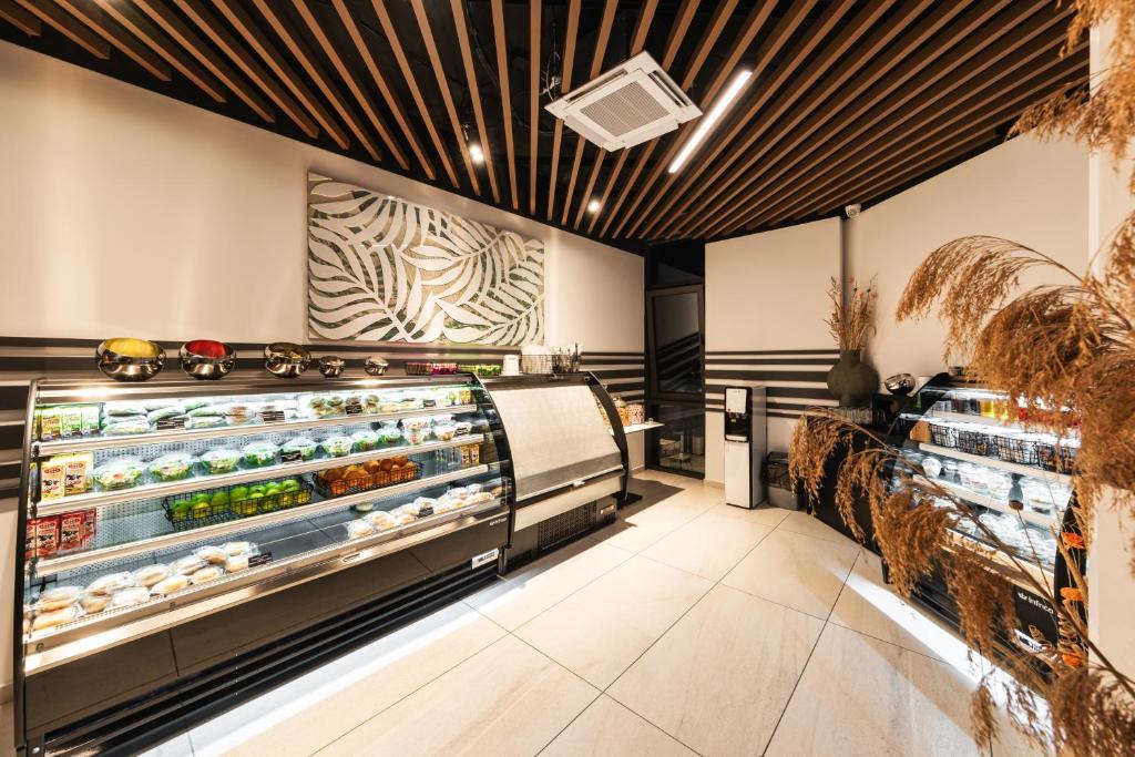 Mūsdienīga veikala iekštelpa ar elegantu dizainu, kurā redzami ledusskapji ar dažādiem produktiem un stilīgs dekoratīvais elements uz sienas.