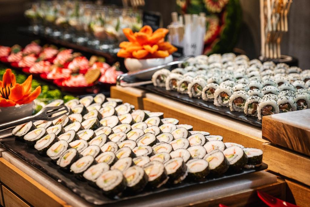 Plaša sushi izvēle uz galda, ar dažādām rullīšu un dārzeņu garnējumu kompozīcijām. Fons papildina ar augļu un dārzeņu dekorācijām.