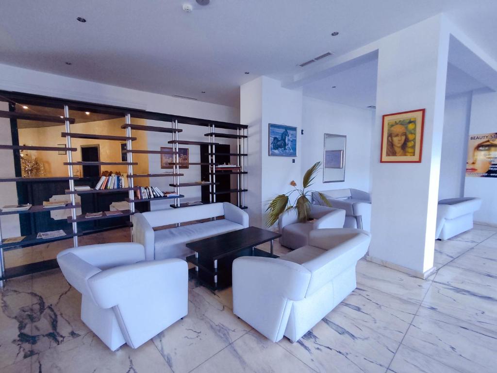 Mūsdienīgs viesnīcas vestibils ar komfortablām baltām mēbelēm, zemu galdiņu un grāmatu plauktu. Uz sienām ir mākslas darbi un dekorācijas, radot patīkamu atmosfēru.