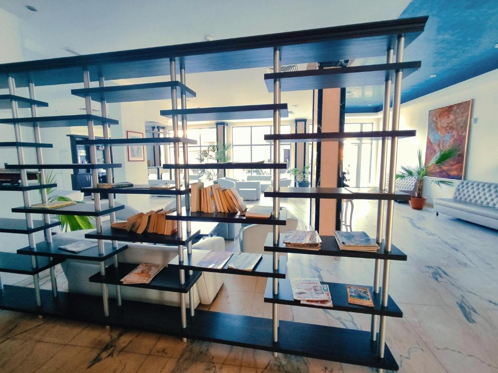 Mūsdienīgs interjers ar grāmatu plauktu un ērtām mēbelēm, kurā redzami augi un gaismas avoti. Telpa ir plaša un gaiša, radot relaksējošu atmosfēru.