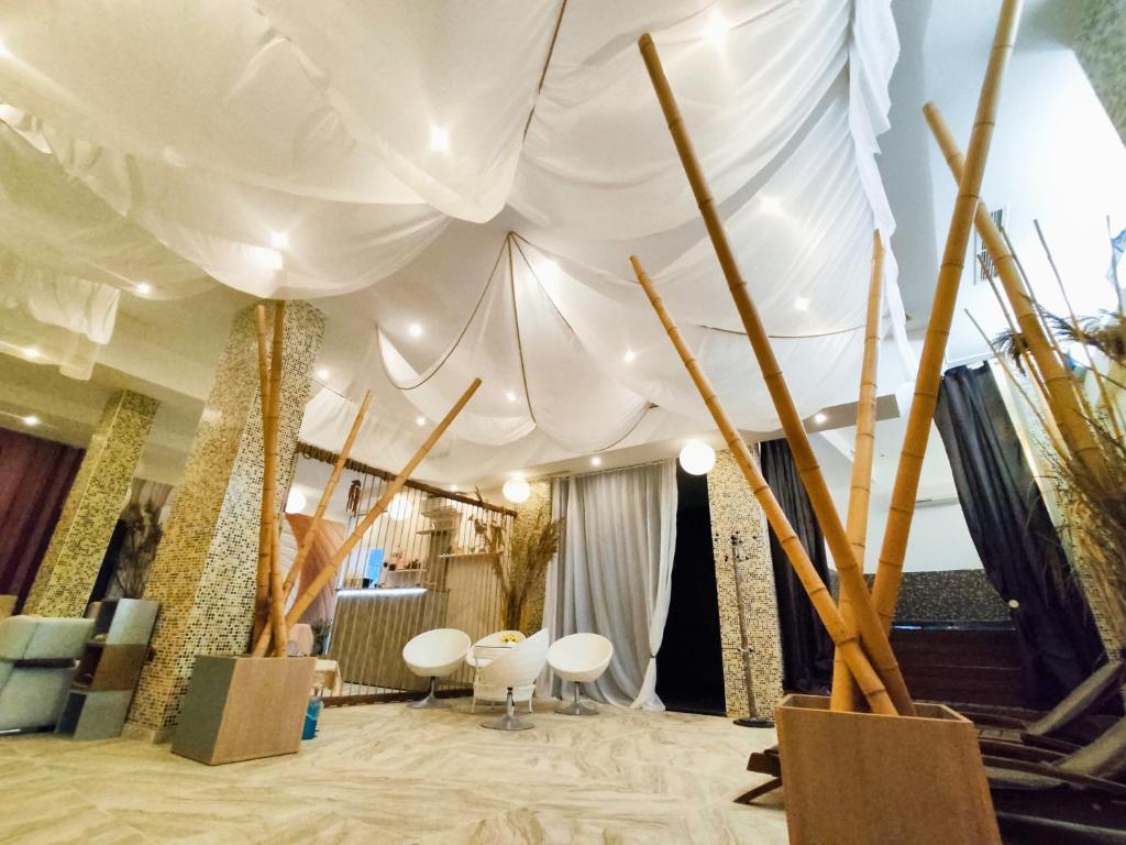 Mūsdienīgs interjers ar baltām drānām pie griestiem un bambusa stabiem, radot relaksējošu atmosfēru. Telpa ir apgaismota ar siltām gaismām, kas piešķir mājīgu noskaņu.