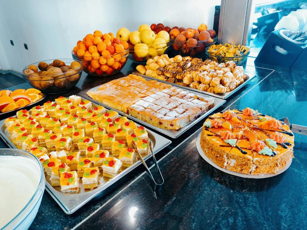 Krāsains desertu galds ar dažādiem kūku un augļu veidiem, tostarp krāsainiem saldumiem, augļu šķīvjiem un krēma trauku.