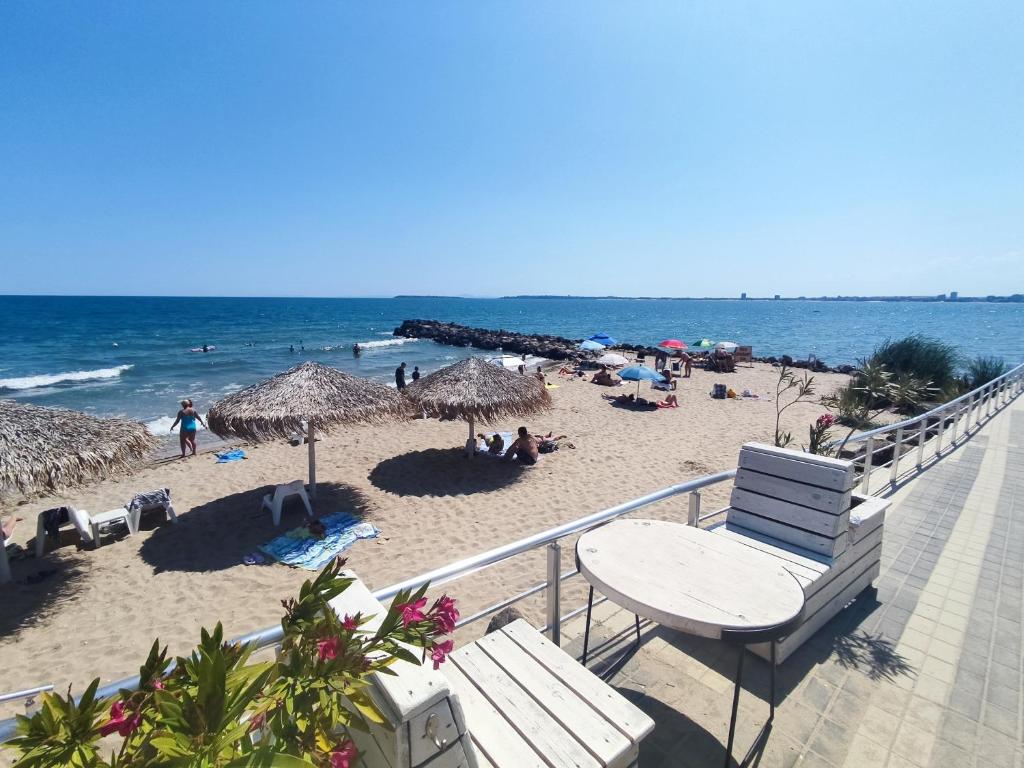 Pludmale ar smiltīm, sauļošanās krēsliem un palmu lapām, kur cilvēki izbauda sauli un jūru. Skats uz zilo okeānu un pludmales aktivitātēm.