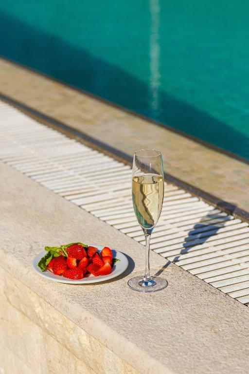 Gaiši zaļš baseins ar glāzi šampanieša un šķīvi ar svaigām zemenēm uz akmens malas.