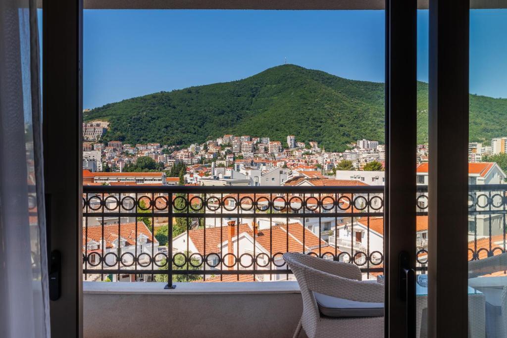 Skats no balkona uz kalnu un pilsētas ainavu, kur redzami jumti ar sarkaniem dakstiņiem un zaļojošs kalns fona.