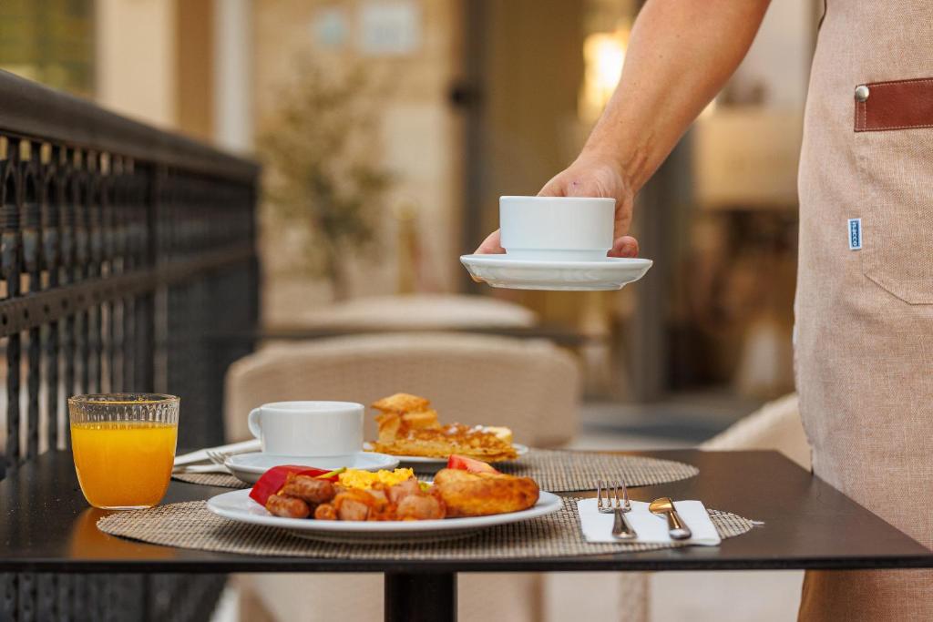 Broka veida galda komplekts ar krūzi, šķīvi un apelsīnu sulu, kurā redzama gardu ēdienu izvēle, ieskaitot olu un desiņas.