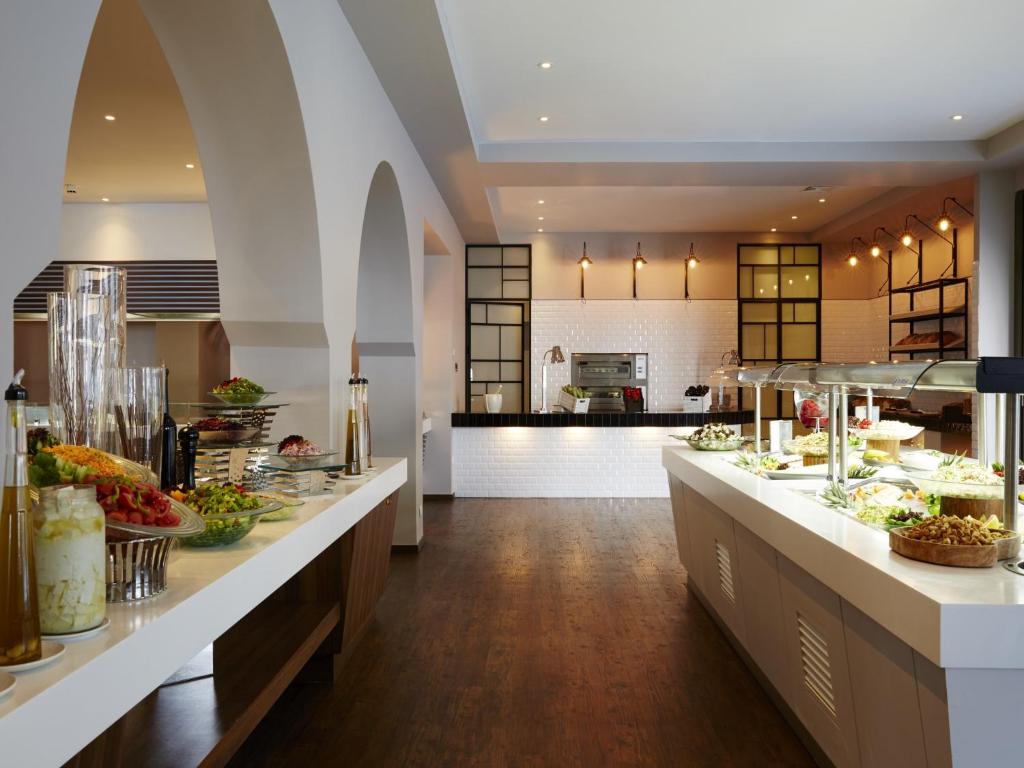 Mūsdienīgs restorāna interjers ar plašu bufeti, kas piedāvā dažādus ēdienus un salātus, izgaismots ar siltu apgaismojumu.