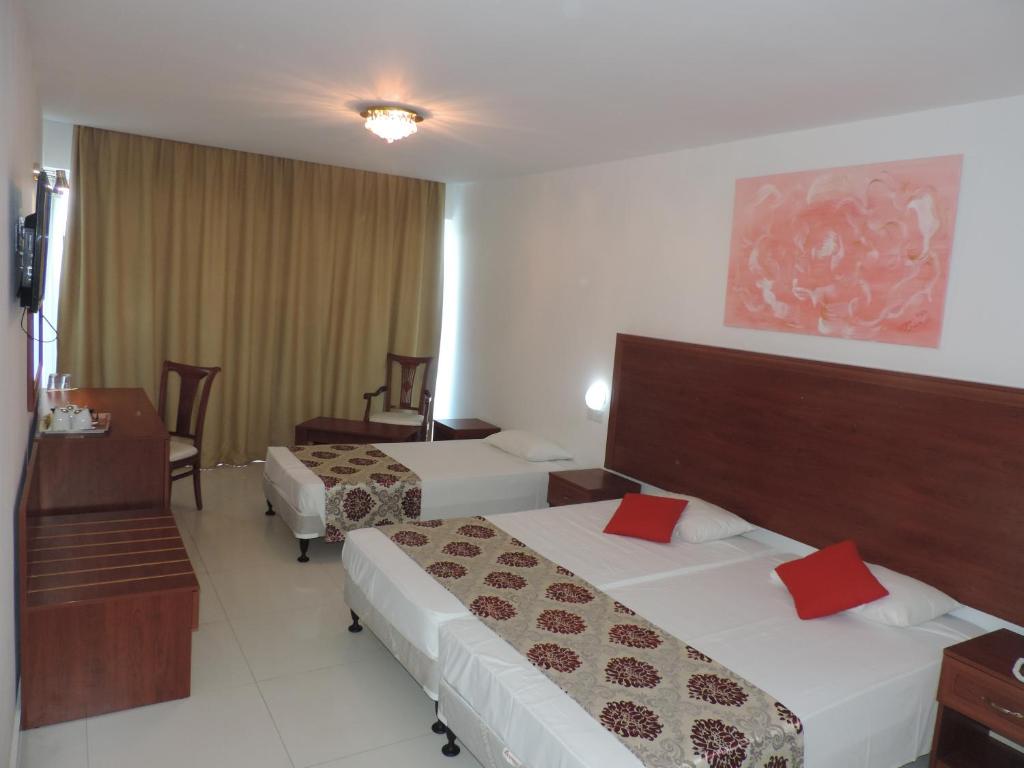 Moderns viesnīcas numurs ar divām gultām, koka mēbelēm un tekstiliju sarkanā un brūnā krāsā, kā arī gaismas elementiem un mākslas darbu uz sienas.