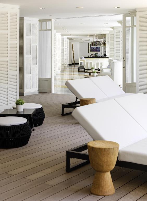 Mūsdienīga atpūtas zona ar baltām sauļošanās gultām un koka sēžamajiem krēsliem, kas rada relaksējošu atmosfēru. Interjers ir gaišs un elegants, ar atvērtām durvīm, kas ved uz bāru.