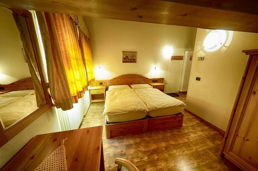 Mājīga guļamistaba ar divām gultām, koka mēbelēm un siltām krāsām, kas rada relaksējošu atmosfēru. Logi ar aizkariem piešķir telpai gaisīgu izskatu.