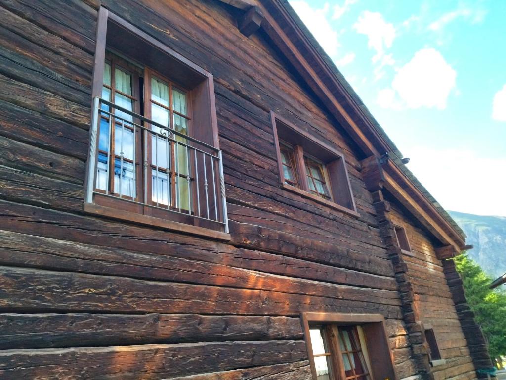 Koka mājas fasāde ar diviem logiem un metāla balkonu, kas atrodas zem zilām debesīm ar mākoņiem.