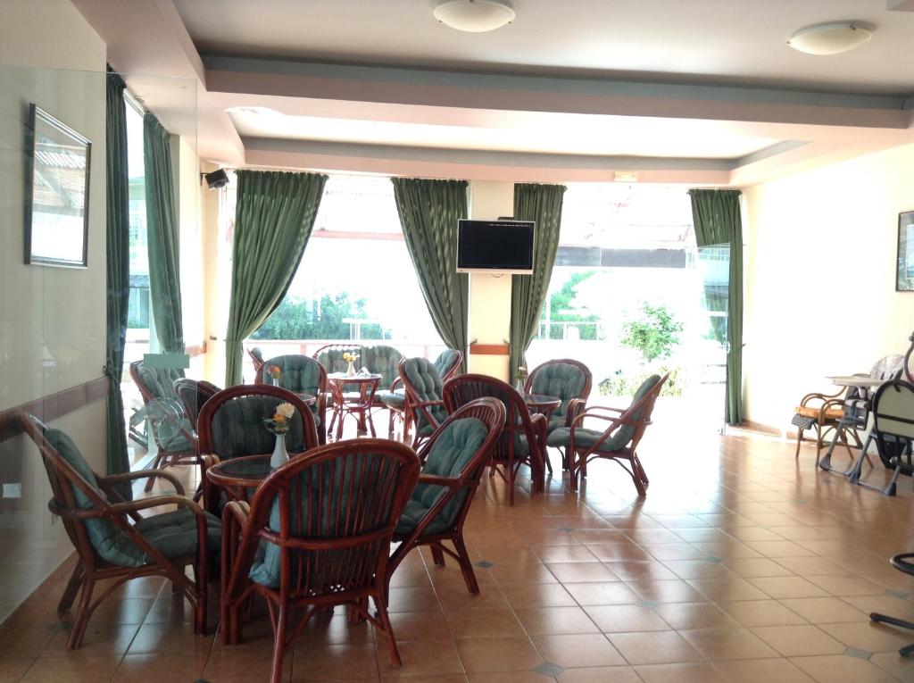 Kafijas telpa ar elegantām mēbelēm, kurā ir vairākas sēdvietas un liels logs, kas ļauj ieplūst dabiskajai gaismai. Interjers ir veidots ar zaļām aizkariem un siltām krāsām, radot relaksējošu atmosfēru.