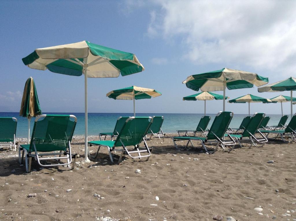 Pludmales ainava ar zaļām sauļošanās krēslām un saulessargiem, kas izklājas pie jūras. Skaidrs zilais debesis un mierīga jūra veido relaksējošu atmosfēru.