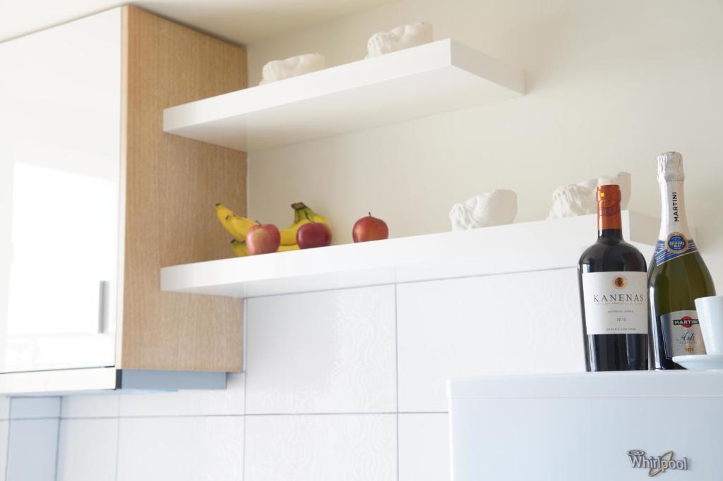 Virtuves interjers ar plauktiem, uz kuriem atrodas augļi un dzērieni, radot mājīgu un modernu atmosfēru. Uz plauktiem izkārtoti āboli, banāni un divas pudeles dzērienu.