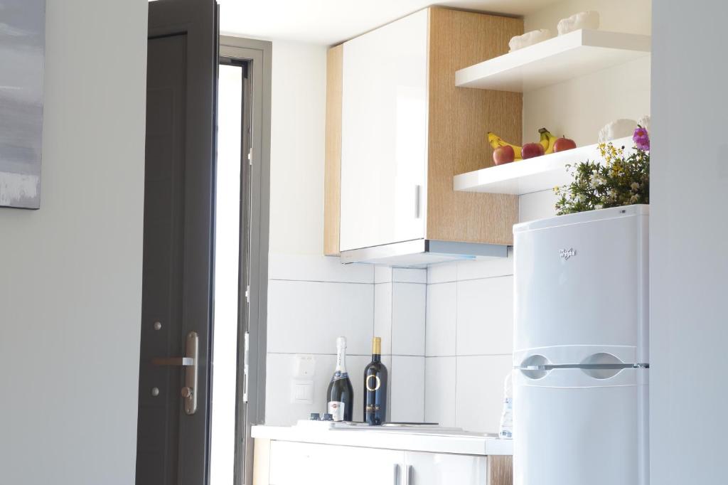 Gaiša virtuve ar baltu ledusskapi un plauktiem, uz kuriem novietotas augļi un ziedi. Virtuves interjers ir moderns un minimālistisks, ar dabīgā koka akcentiem.