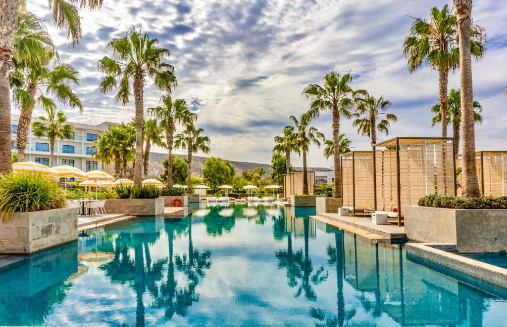 Luksusa viesnīcas baseins ar palmām un saulessargiem, kas atspoguļojas ūdenī, radot mierīgu un relaksējošu atmosfēru. Ideāla vieta atpūtai un izklaidei.