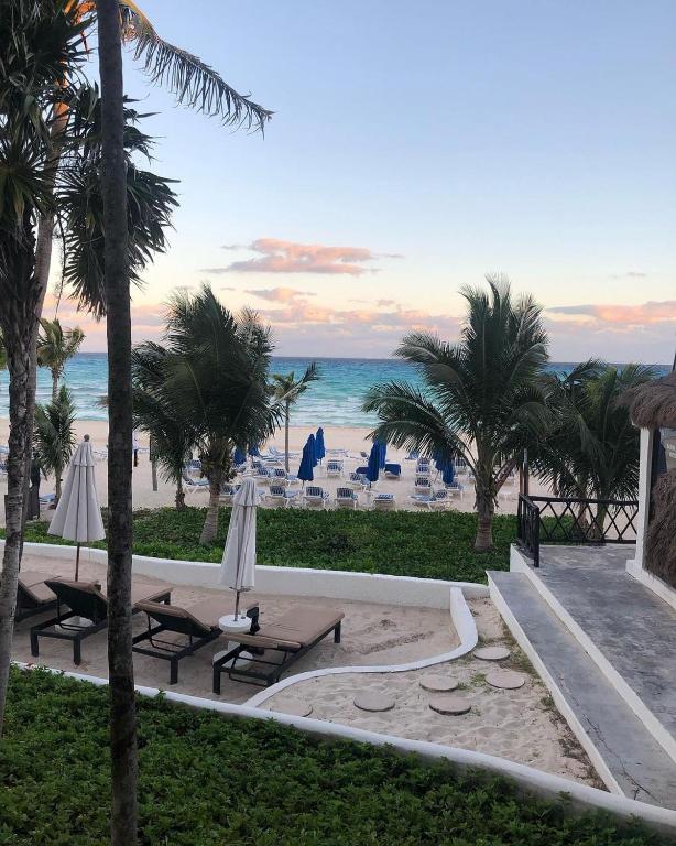 Pludmales skats ar palmām, saulessargiem un sauļošanās krēsliem, zilām jūras viļņiem un debesīm, kas apmākušās.