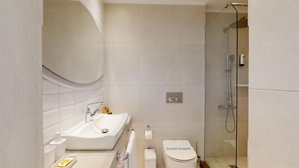 Mūsdienīgs vannas istabas interjers ar stūra izlietni, lielu spoguli un dušas kabīni. Neitrālas krāsas un minimālistisks dizains rada patīkamu atmosfēru.