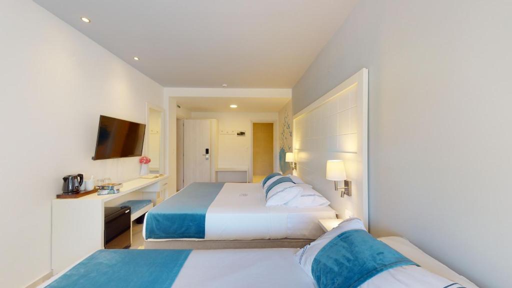 Mūsdienīgs viesnīcas numurs ar divām gultām, TV un ērtu mēbeļu komplektu. Telpa ir gaiša un eleganta, ar zilu un baltu krāsu kombināciju.