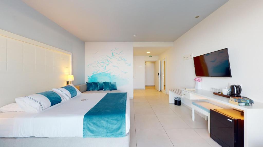 Mūsdienīgs viesnīcu numurs ar gaišām krāsām, ērku gultu un dekoratīvām spilveniem. Interjerā ir televizors, galds un krēsli, kā arī eleganta sienu glezna.