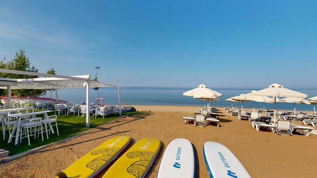 Pludmales skats ar saulessargiem un atpūtas krēsliem, kā arī dēļu sērfošanai. Miers un skaists skaidrs debesis virs ūdens.